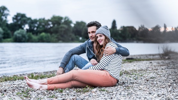 Mann und Frau sitzen Arm in Arm am Ufer eines Flusses