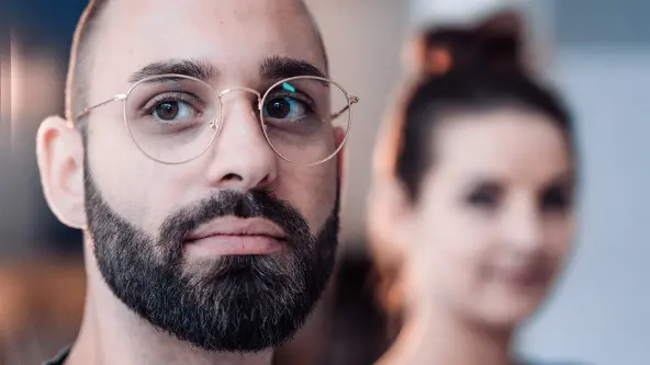Mann schaut mit ernstem Blick in die Kamera und hinter ihm ist eine Frau