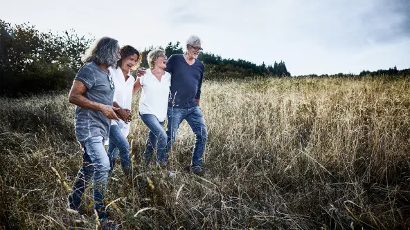 4 ältere Personen laufen lachend durch ein hoch bewachsenes Feld