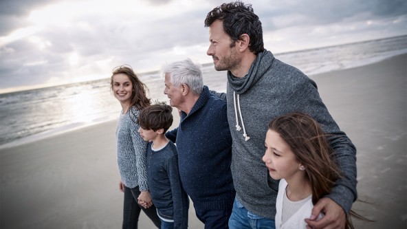 Familie mit 2 Kindern und Großvater läuft Arm in Arm am Strand entlang