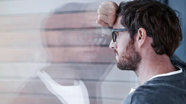 Mann mit Brille und Bart lehnt nachdenklich an einer Glasscheibe