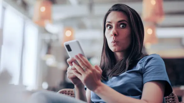 Junge Frau zieht ihre Lippen zusammen und hat ein Smartphone in der Hand