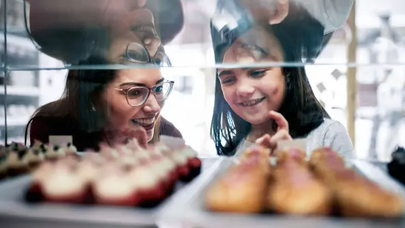 Mutter und Tochter betrachten lächelnd die Auslage in einer Bäckerei