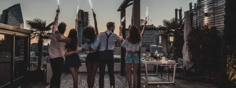 Fünf junge Menschen halten auf Dachterrasse ein Tischfeuerwerk in die Luft