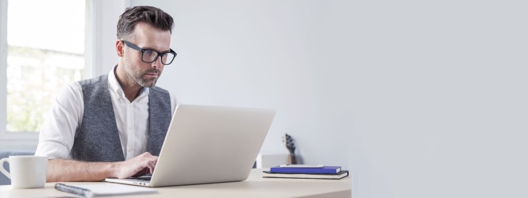 Mann mit schwarzer Brille sitzt an Tisch und arbeitet am Laptop