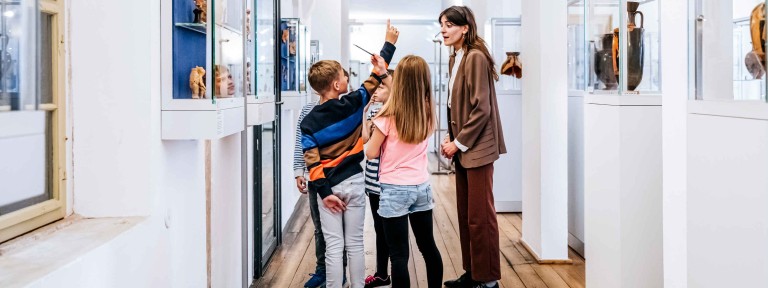 Frau steht mit 4 Kindern in einem Museum