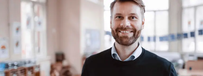 Junger Mann steht mit einem Lächeln in einem Türrahmen von einem Klassenzimmer