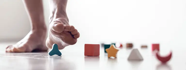 Ein Mann tritt Barfuß auf ein paar herrumliegende Spielzeugbausteine