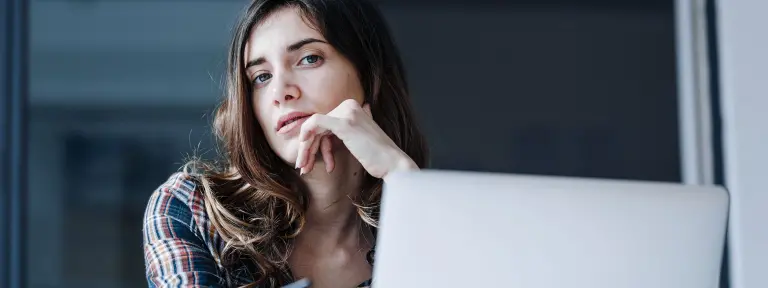 Frau sitz vor Notebook und schaut nachdenklich