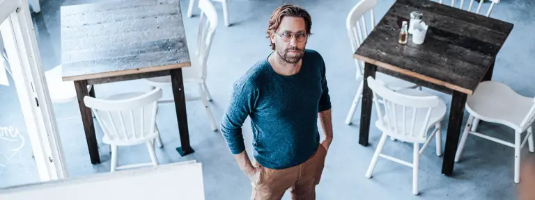 Mann mit Brille steht in einem Raum voller Tische und Stühle und blickt nach oben