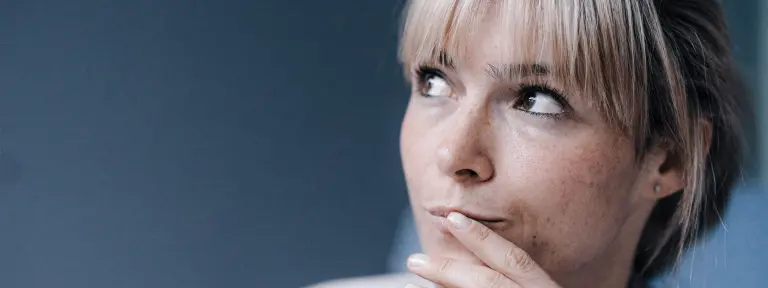 Junge Frau hält die Hand Hand an den Mund und blickt zur Seite