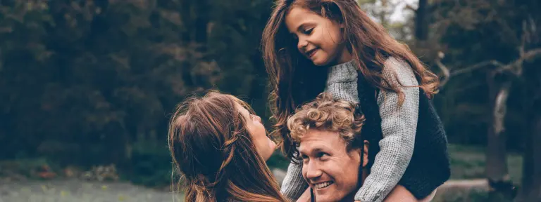 Junger Mann hat Mädchen mit langen Haaren auf Schulter und vor ihnen steht eine junge Frau