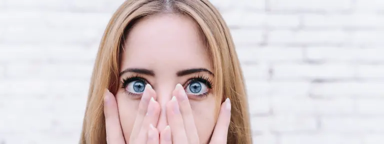Junge Frau hält sich beide Hände vor den Mund und man sieht ihre blauen Augen