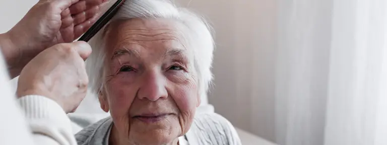 Ältere Frau mit weißen Haaren wird von einer anderen Person gekämmt