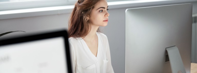 Junge Frau mit dunklen Haaren sitzt konzentriert vor einem großen Monitor