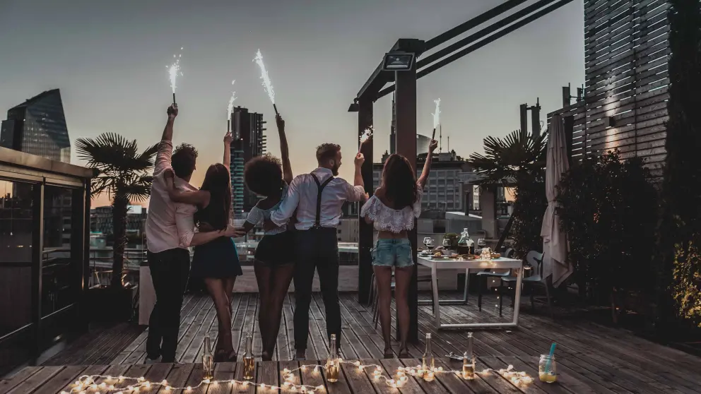 Fünf junge Menschen halten auf Dachterrasse ein Tischfeuerwerk in die Luft