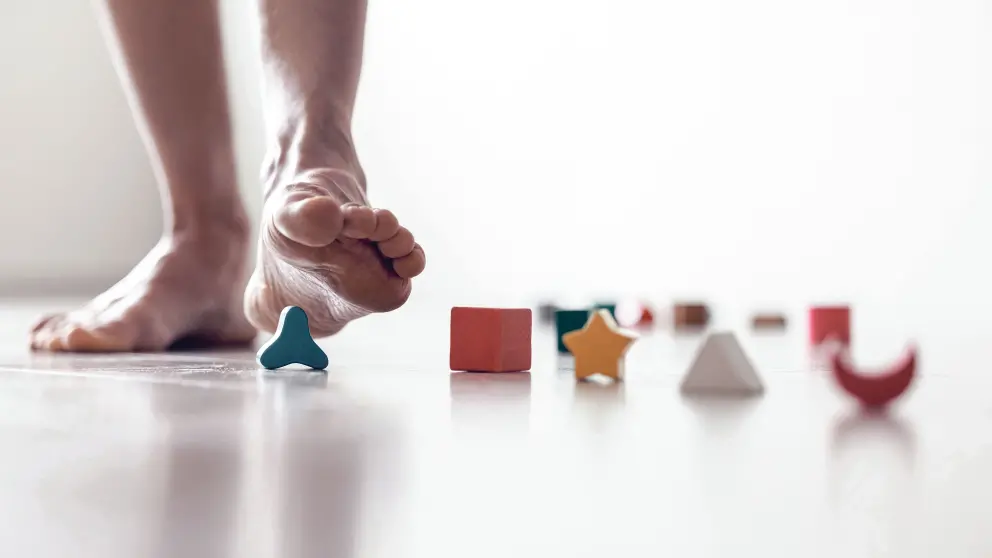 Ein Mann tritt Barfuß auf ein paar herrumliegende Spielzeugbausteine