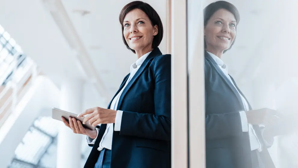 Frau lehnt mit Tablet in der Hand an einer Wand