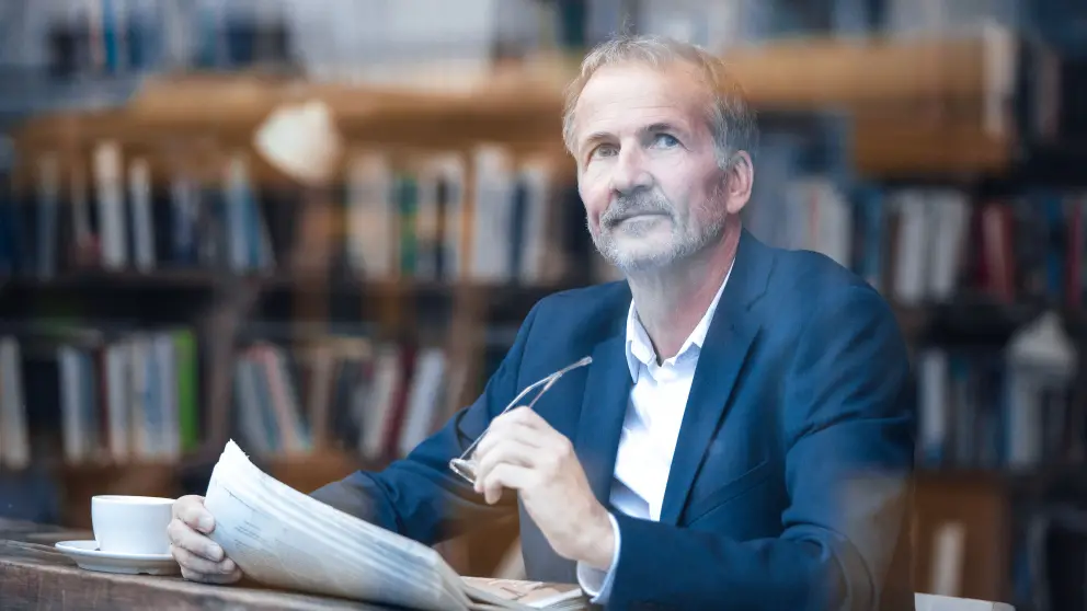 Mann mittleren Alters liest Zeitung und schaut nachdenklich aus dem Fenster
