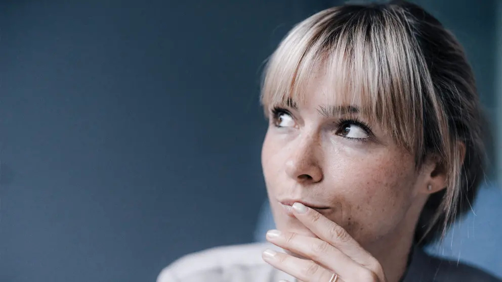 Junge Frau hält die Hand Hand an den Mund und blickt zur Seite