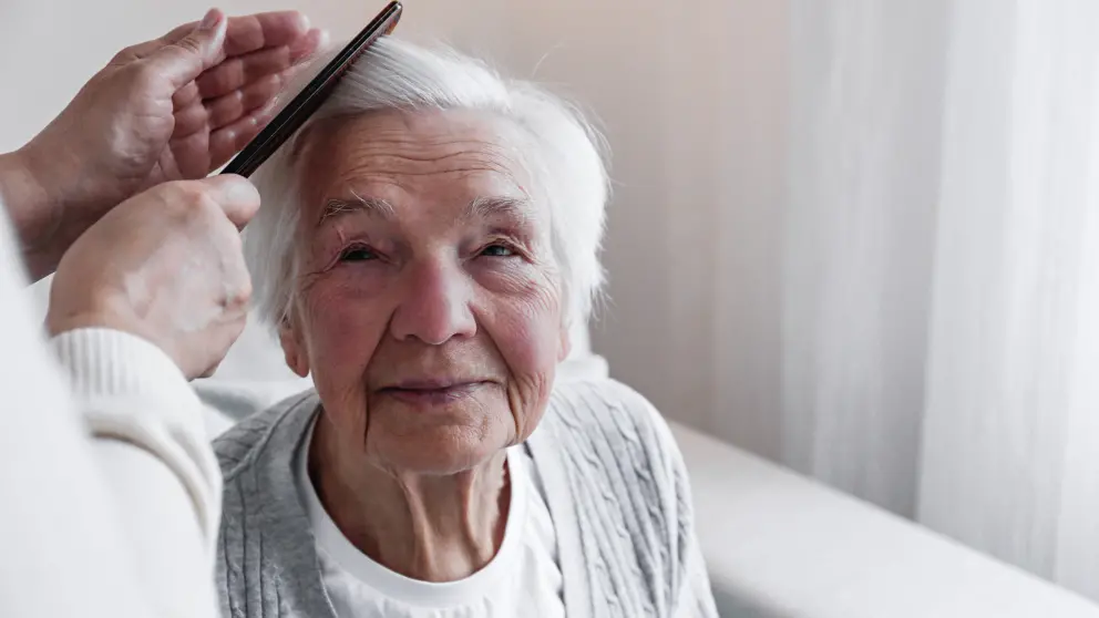 Ältere Frau mit weißen Haaren wird von einer anderen Person gekämmt