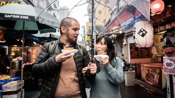 Mann und Frau laufend mit einem Brötchen in der Hand durch einen asiatischen Markt