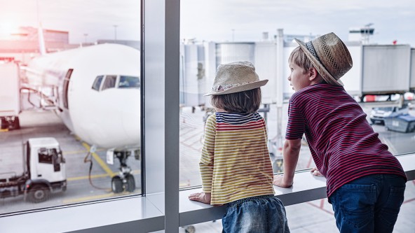 2 kleine Kinder mit Hut auf dem Kopf schauen sich am Flughafen Flugzeuge an