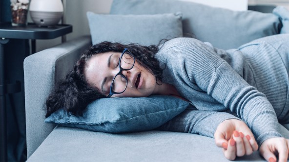 Frau mit dunkler Brille liegt schlafend auf einer Couch
