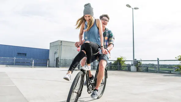 Junges Mädchen sitzt auf Lenker eines Fahrrads, welches von einem Jungen gefahren wird