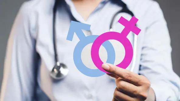 Eine Person mit blauem Hemd und Stethoskop hält die Symbole für Mann und Frau vor der Brust