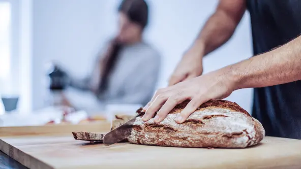 Mann schneidet Scheiben von einem Brot ab