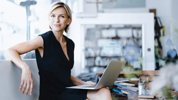 Frau mit blonden Haaren und schwarzem Kleid hat Laptop auf dem Schoß