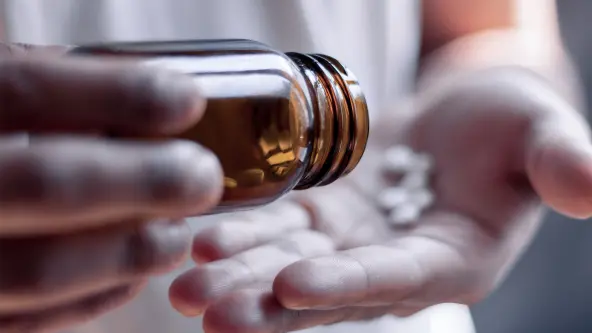 Person schüttet mehrere weiße Tabletten auf Handfläche aus