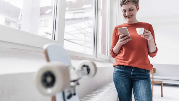 Junge Frau mit kurzen Haaren schaut auf ihr Handy, während sie einen Espresso trinkt und zu ihrem Skateboard geht