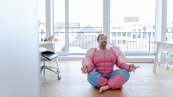 Mann in pinkem Superheldenkostüm sitzt meditierend am Boden