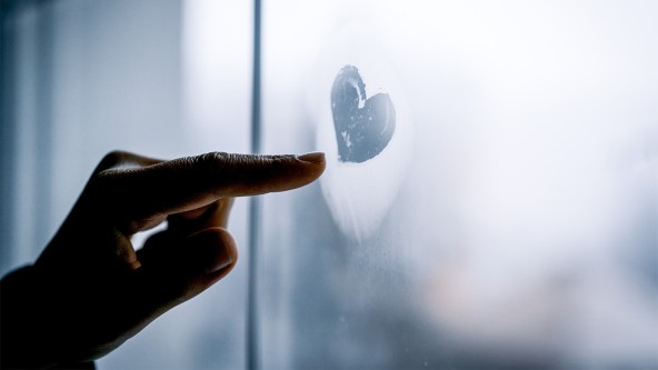 Eine Hand malt ein Herz auf eine angelaufene Fensterscheibe
