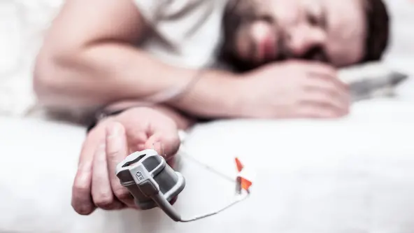 Mann liegt mit einem Messgerät am Finger in einem Bett