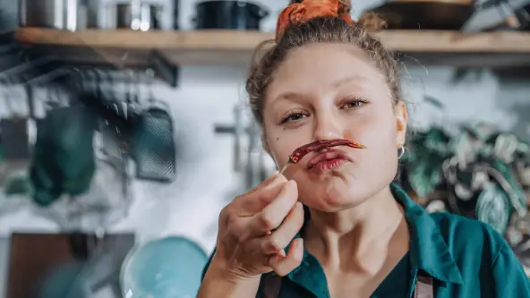 Eine junge Frau hält sich eine Chili vor den Mund