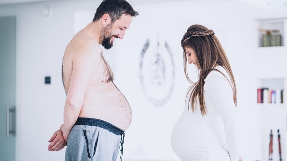 Mann mit runden Bauch steht Frau mit rundem Schwangerschaftsbauch gegenüber