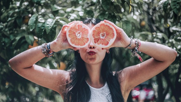 Frau hält sich 2 aufgeschnittene Hälften einer Grapefruit vor die Augen