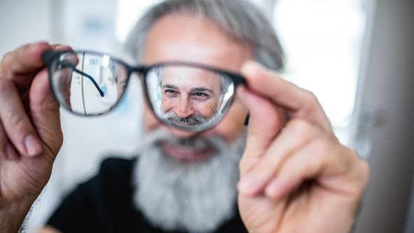 Älterer Mann mit Bart hält sich seine Brille vor sein Gesicht
