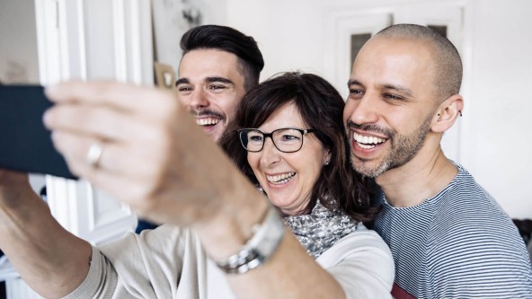 Frau macht ein Selfie von sich und 2 Männern, die neben ihr stehen