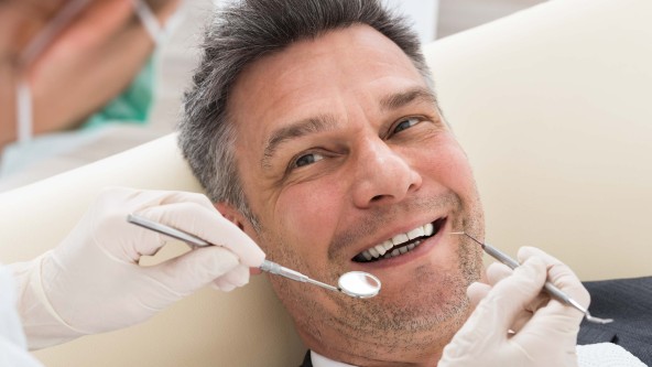 Mann mittleren Alters sitzt auf Behandlungsstuhl beim Zahnarzt