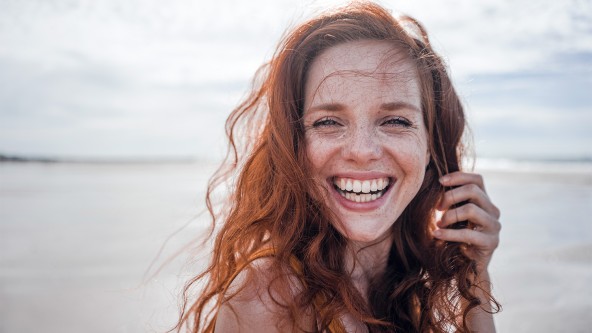 Rothaarige Frau steht lachend am Strand