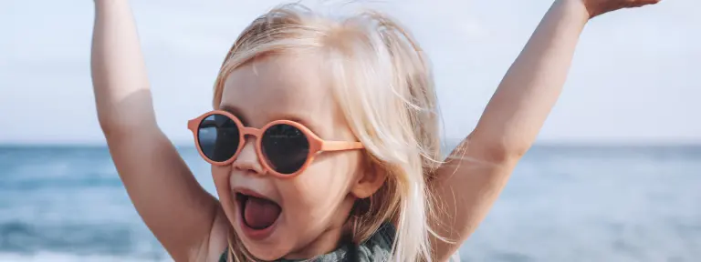 Junges Mädchen mit Sonnenbrille streckt lachend die Arme in die Luft
