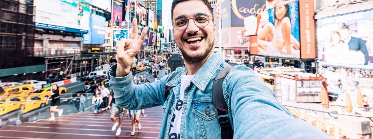 Mann mit Brille steht am Times Square und macht ein Selfie