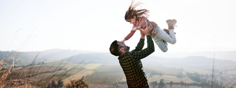 Vater wirft auf einer Wiese seine Tochter in die Luft