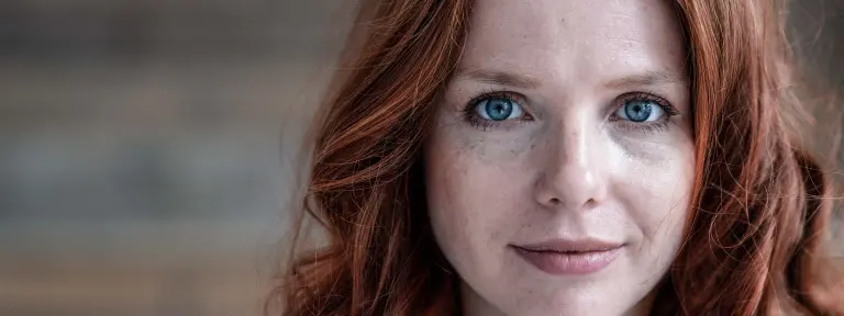 Junge rothaarige Frau schaut mit ihren blauen Augen direkt in die Kamera