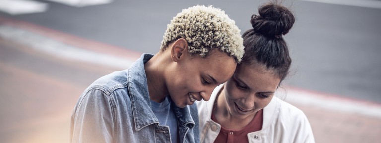 2 junge Frauen blicken gemeinsam lachend in ein Smartphone