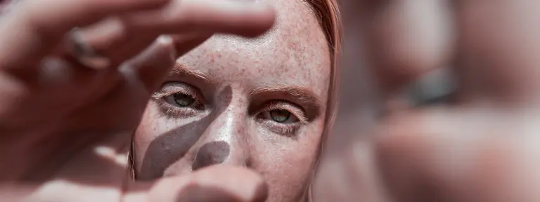 Frau mit Sommersprossen schaut durch ihre eigene Hand